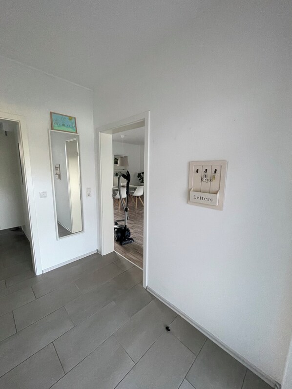 A hallway with a vacuum cleaner, a mirror, and a wall-mounted light switch.