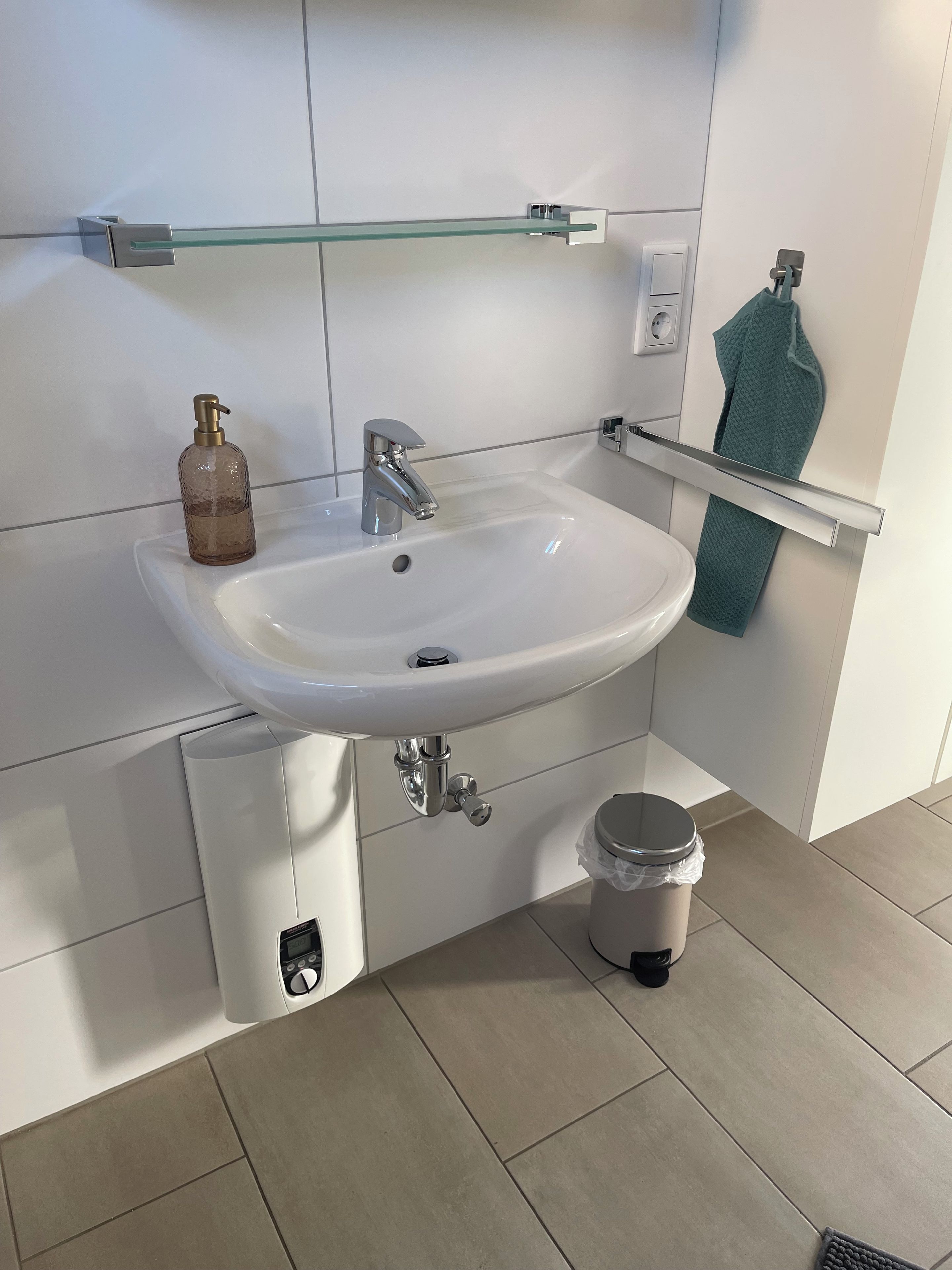Een moderne badkamer met een wit wastafel, een chromen kraan en een glazen plank erboven.