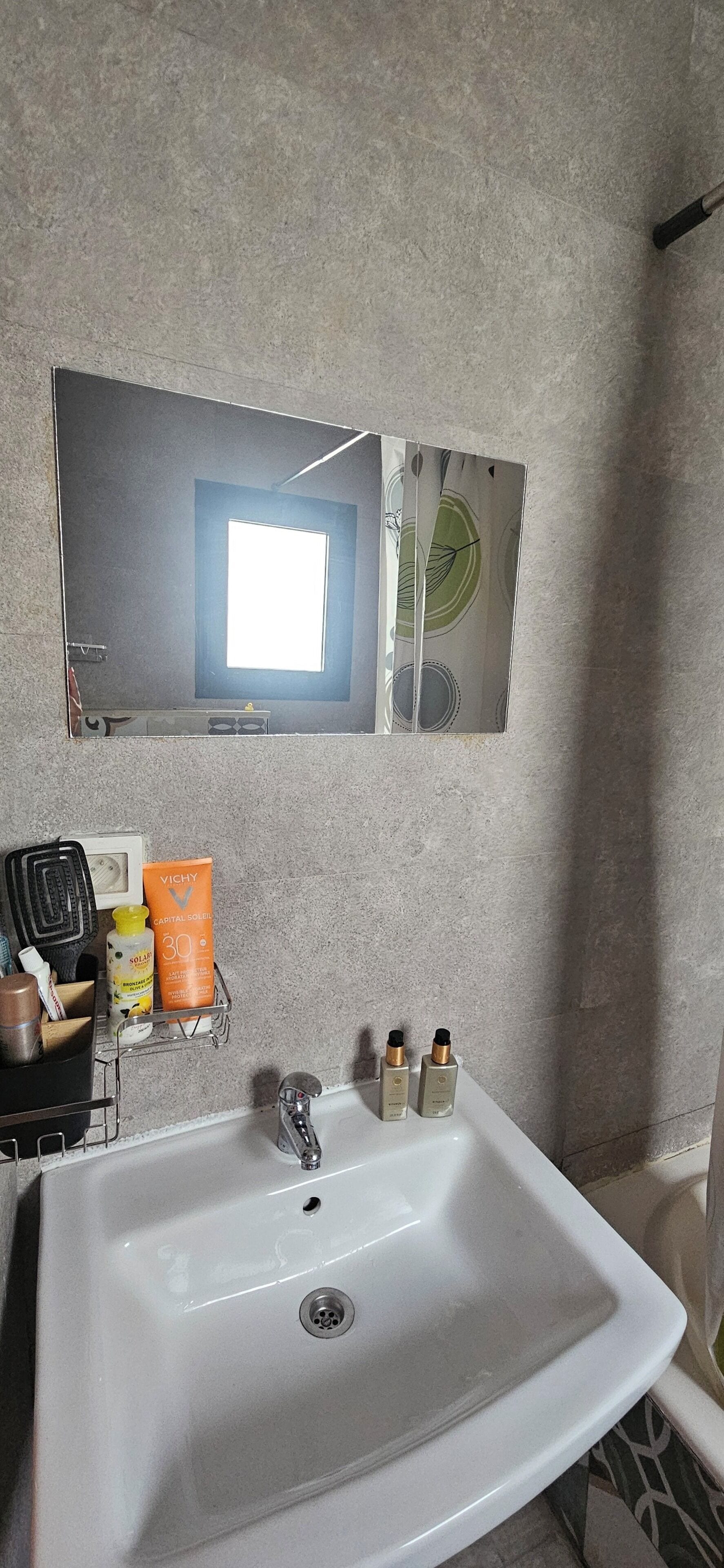 A bathroom with a white sink, a mirror, and toiletries.