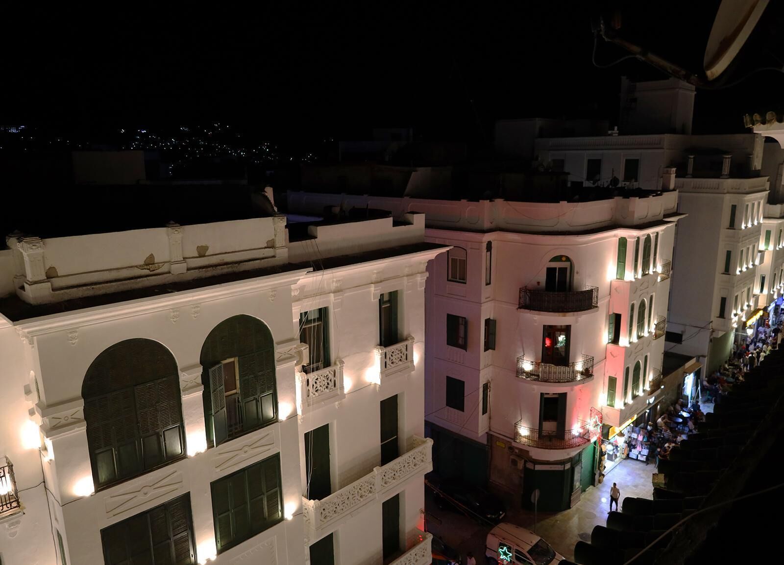 A row of white buildings with balconies, some with lights on, and a street below.