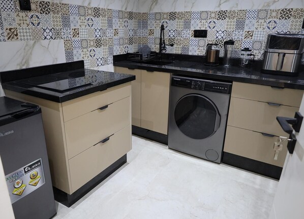 A compact kitchen with a washing machine, a stove, and a coffee maker.