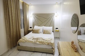 A hotel room with a large bed, bedside tables, a mirror, and curtains.
