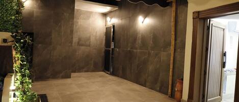 A room with a tiled floor, a green artificial turf area, a wall-mounted light fixture, and a door with a wooden frame.