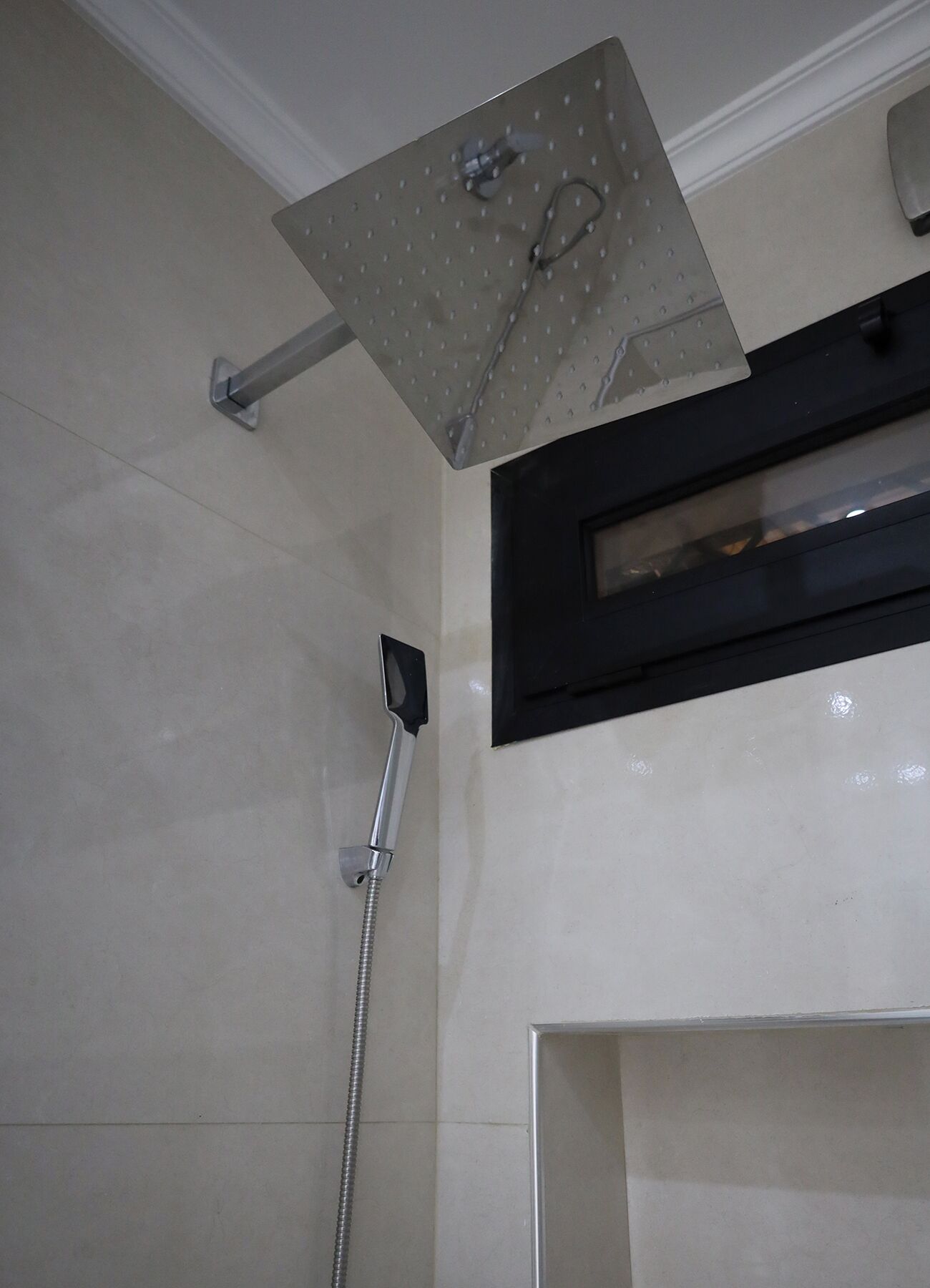 Un espacio de ducha con cabezal de ducha manual y panel de control en la pared.