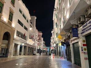 A nighttime street with buildings, some shops, and a few pedestrians.