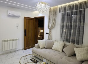 A modern living room with a sofa, a glass coffee table, a chandelier, and a radiator.