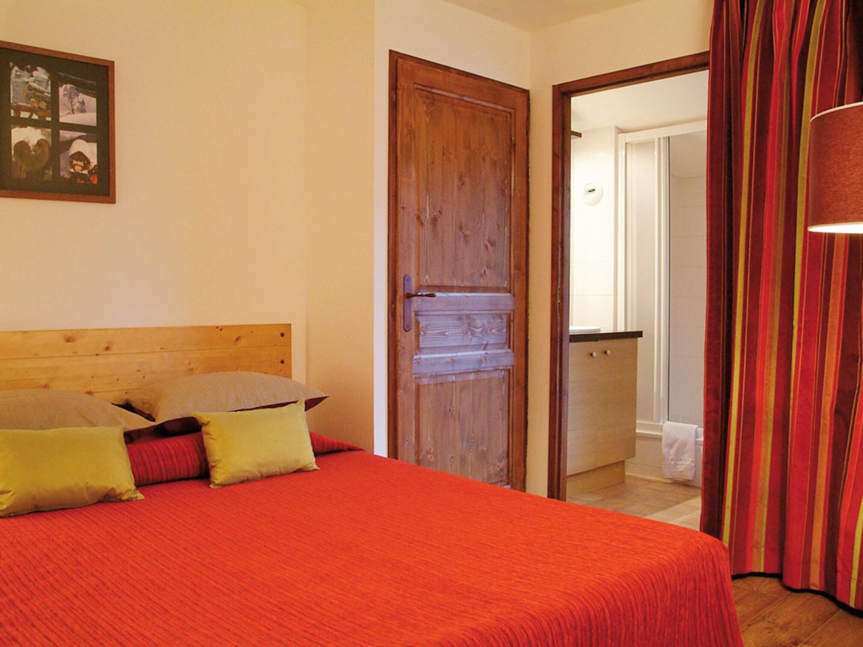 A bedroom with a wooden headboard, a bed with red bedding, and a door leading to a bathroom.