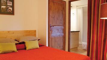A bedroom with a wooden headboard, a bed with red bedding, and a door leading to a bathroom.