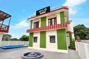 Ein Hotel, das von Oyo bewirtschaftet wird, erkennbar am Schild. Es handelt sich um ein zweistöckiges Gebäude mit einem Pool und einem runden Wasserspiel im Vordergrund.