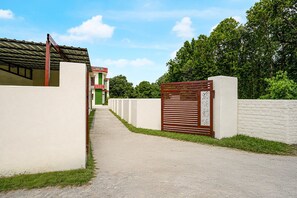 A gated entrance with a pathway leading to a building with a green and white facade. - Classic Nautiyal Home Stay (Vikasnagar)