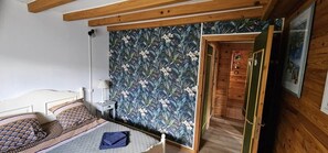 A bedroom with a bed, a nightstand, a wall with a floral pattern, and a door leading to another room.