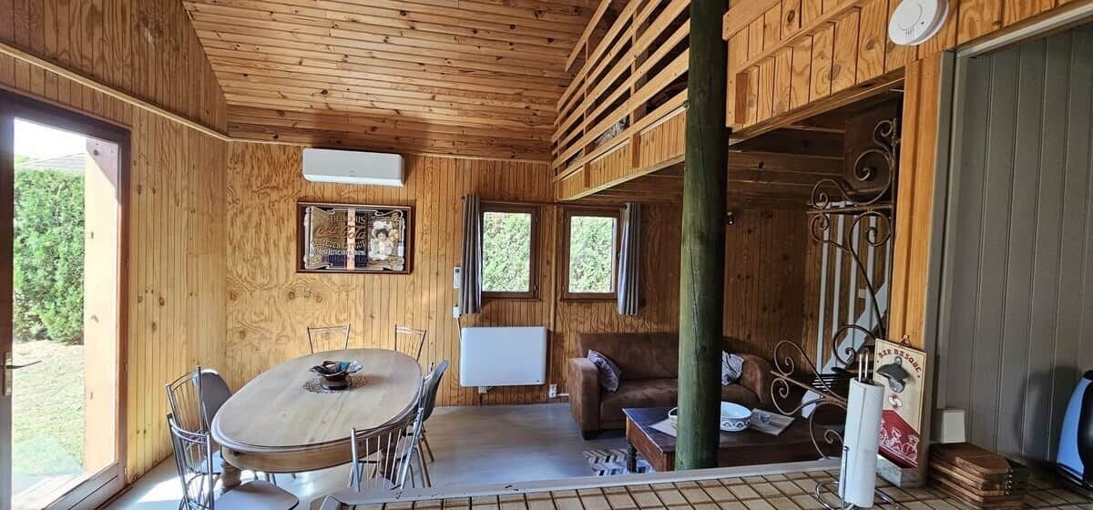Een houten cabin interieur met een eettafel, stoelen, een bank en een raam.