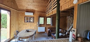 A wooden cabin interior with a dining table, chairs, a sofa, and a window.