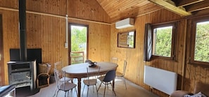 A wooden interior with a round table, chairs, a fireplace, and windows.