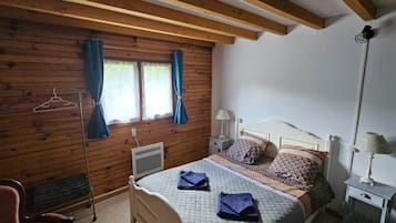 A bedroom with a bed, bedside tables, a chair, a heater, and a window with curtains.