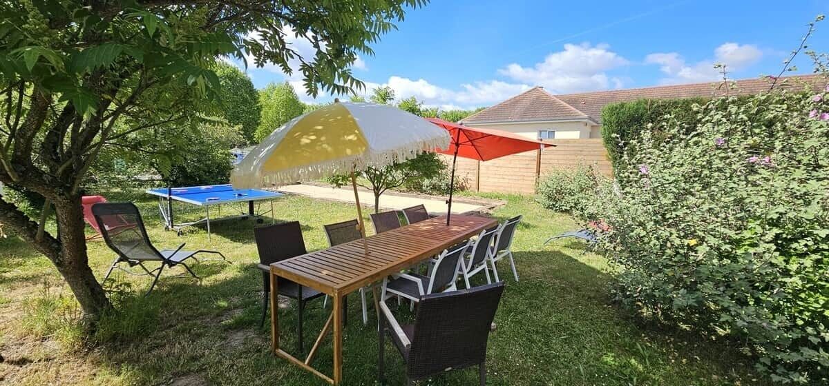 An outdoor patio with a wooden table and chairs, a yellow and white umbrella, and a red umbrella.