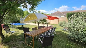 An outdoor patio with a wooden table and chairs, a yellow and white umbrella, and a red umbrella.