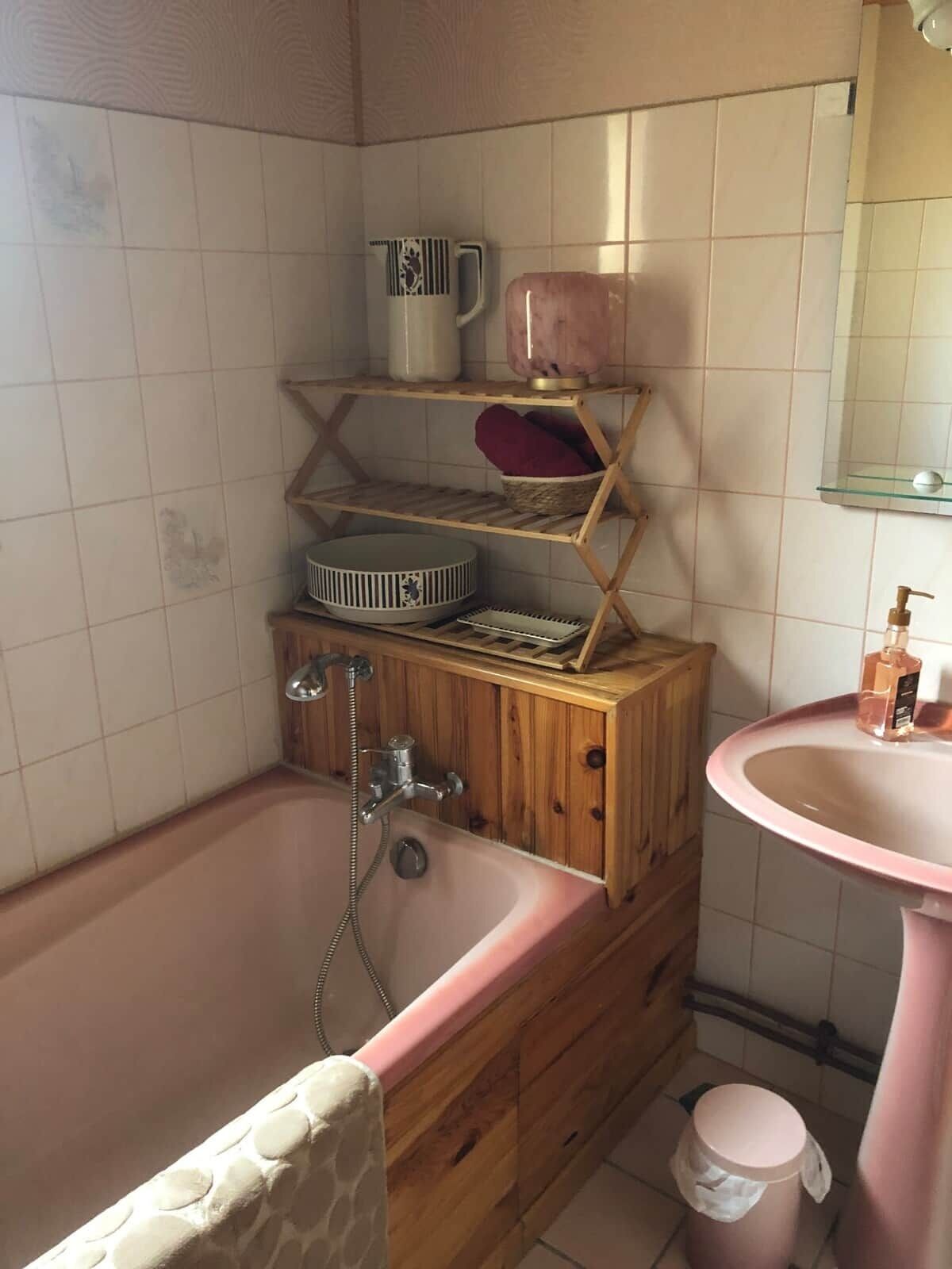 Un baño con tocador de madera, lavamanos rosa y bañera.