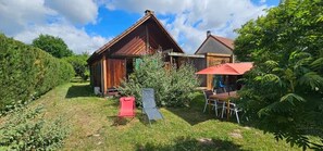 A rustic wooden cabin with a red roof, surrounded by lush greenery and a clear sky.