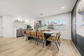 A modern kitchen with white cabinets, a dining area with a round table and chairs, and a large window with blinds. - NEW| The Fairmont @ Kierland | Pool, Spa & Daybeds (Scottsdale)