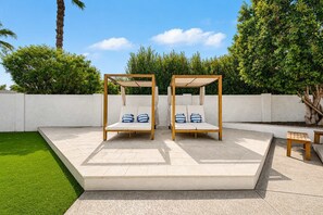 Two wooden swing beds with cushions, a white wall, and a small table in a garden setting. - NEW| The Fairmont @ Kierland | Pool, Spa & Daybeds (Scottsdale)