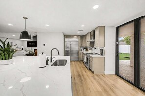 A modern kitchen with a marble countertop, stainless steel appliances, and a sliding glass door to the outdoors. - NEW| The Fairmont @ Kierland | Pool, Spa & Daybeds (Scottsdale)