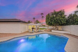 A swimming pool with lounge chairs and umbrellas, surrounded by a landscaped yard with trees and a white wall. - NEW| The Fairmont @ Kierland | Pool, Spa & Daybeds (Scottsdale)