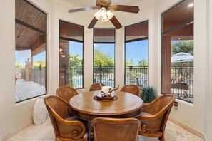 A dining area with a round table, six wicker chairs, a ceiling fan, and large windows with a view of a pool and greenery. - Desert Vista Off-Road Experience|E-Dirt Bikes|Pool (Scottsdale)