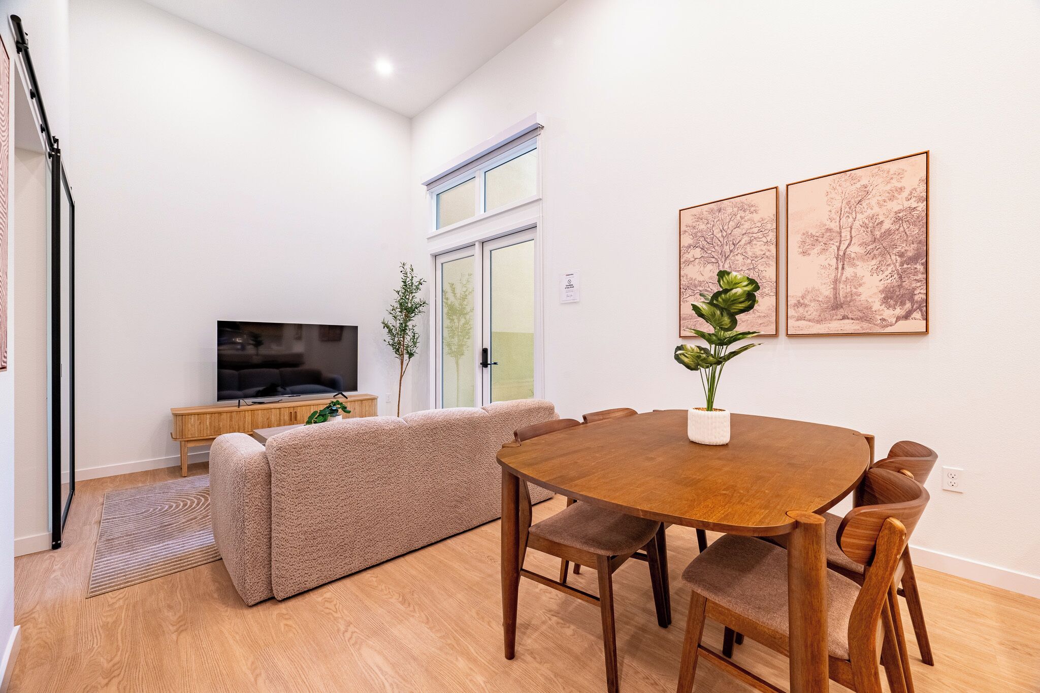 Una sala de estar moderna con un sofá, una mesa de comedor, sillas, un televisor y obras de arte enmarcadas en la pared.