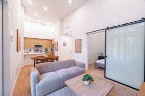 A modern living space with a sofa, dining table, kitchen area, and a sliding glass door.