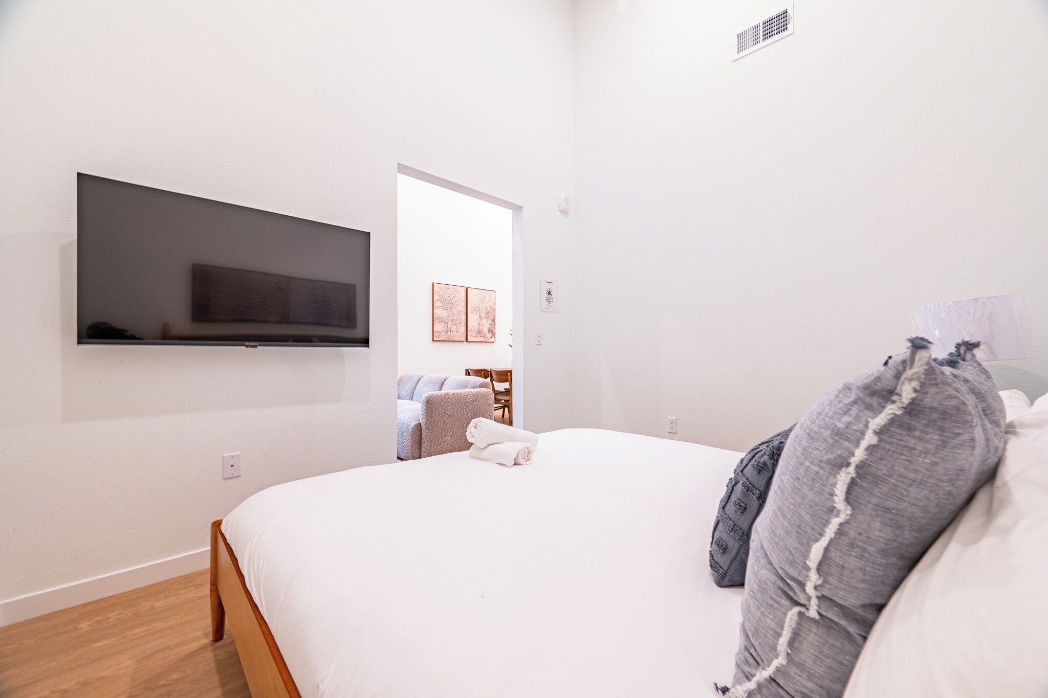 Ein modernes Hotelzimmer mit einem Bett, einem flachbildfernseher an der Wand, einer kleinen Sitzecke mit Sofa und Sesseln sowie einer Tür zu einem weiteren Raum.