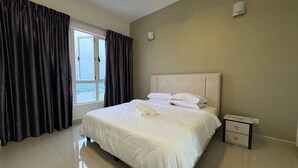 A hotel room with a large bed, a nightstand, a window with curtains, and a view of the outdoors. - Spacious Stay at Danga Bay - Entire Unit (Johor Bahru)