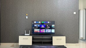 A modern living room with a flat-screen TV mounted on a textured wall, a white router, and two wooden side tables. - Spacious Stay at Danga Bay - Entire Unit (Johor Bahru)