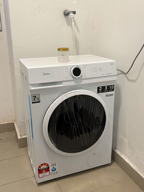 A front-loading washing machine with a control panel, a water inlet, and a label indicating a 7.5 kg capacity. - Spacious Stay at Danga Bay - Entire Unit (Johor Bahru)