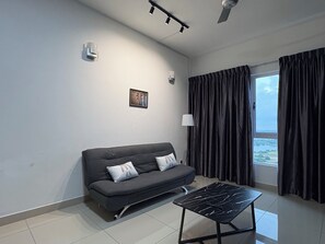 Un salon moderne avec un canapé gris, une table basse noire, une fenêtre avec des rideaux et un tableau accroché au mur.