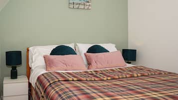 Een bed met een geruite plaid, twee kussens en twee bedlampen.