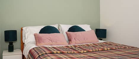 Una cama con colcha a cuadros, dos almohadas y dos lámparas de noche.
