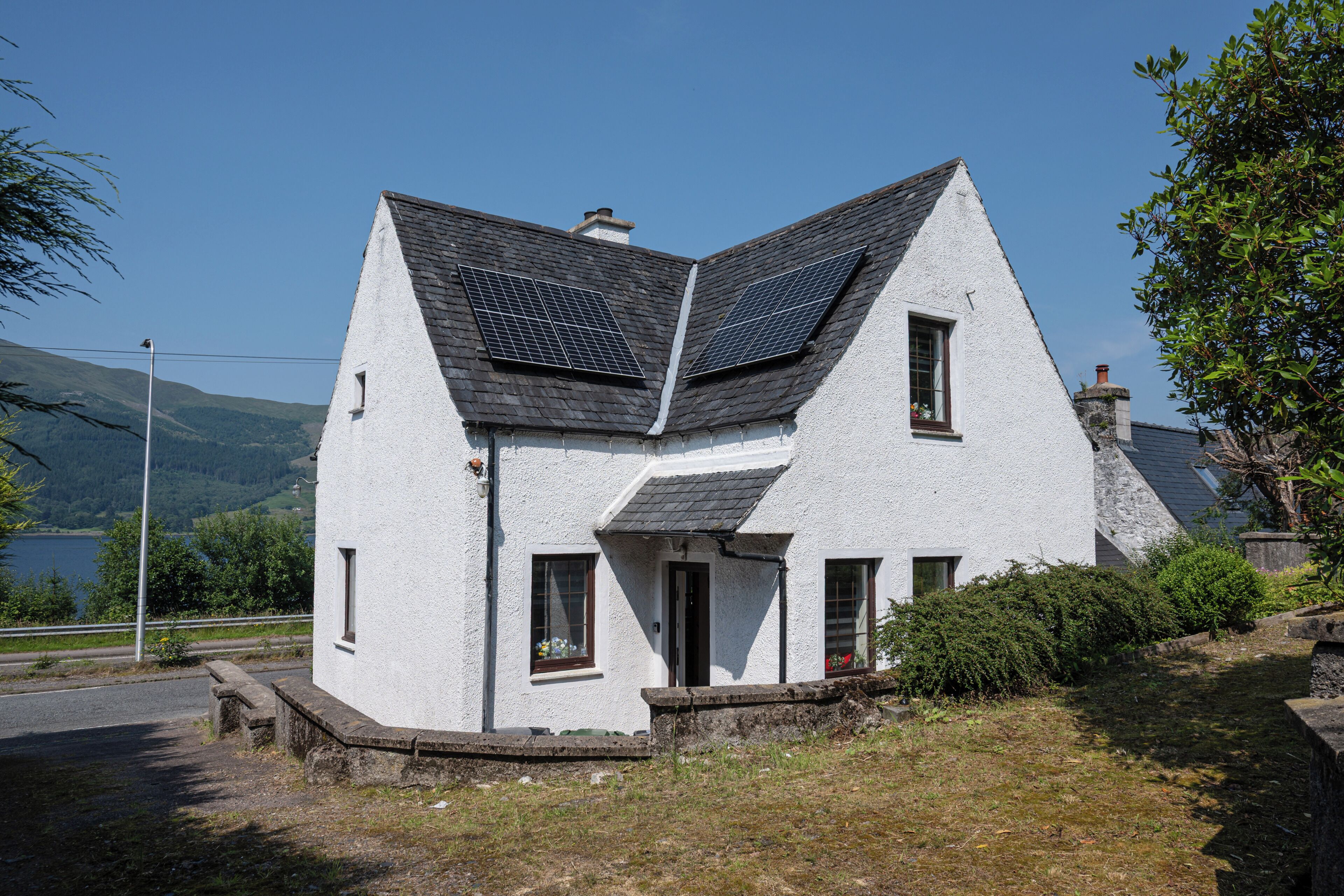 A white house with a steeply pitched roof, solar panels, and a small garden.