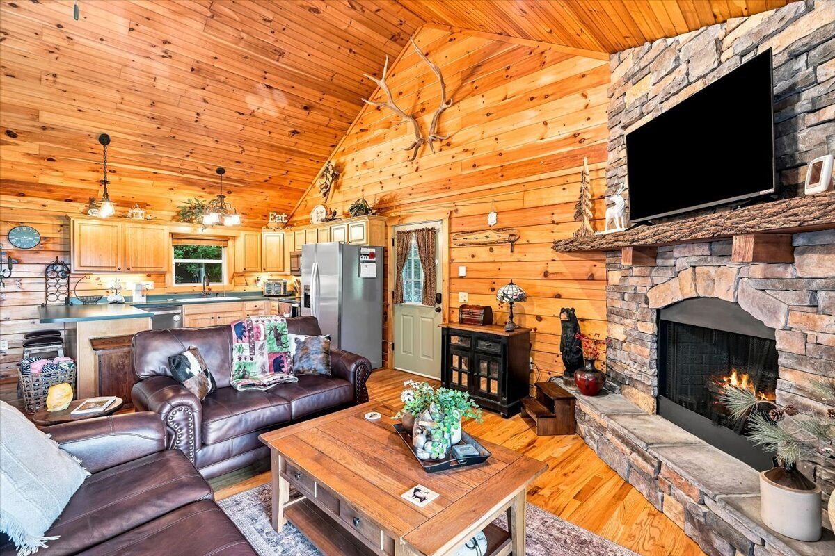 A log cabin interior with a stone fireplace, leather sofa, and a kitchen area.