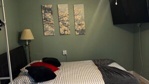 En säng med mönstrat sänglinne, en lampa och tre tavlor som hänger på väggen.