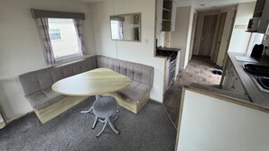 A compact living space with a kitchenette, a dining area with a table and bench, and a small seating area. - Explore Flamborough & Beyond: Comfy Caravan on Action-Packed Haven Site (Flamborough)