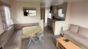 A compact living space with a sofa, a small table, a kitchenette, and a window. - Explore Flamborough & Beyond: Comfy Caravan on Action-Packed Haven Site (Flamborough)
