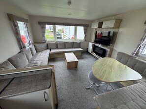A compact living space with a sofa, a small table, a kitchenette, and a television. - Explore Flamborough & Beyond: Comfy Caravan on Action-Packed Haven Site (Flamborough)