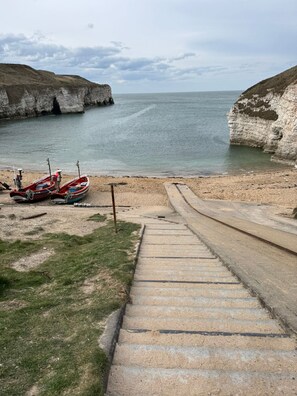Eine Küstenansicht mit einer Treppe, die zu einem Strand führt, Booten im Hafen und Klippen im Hintergrund.