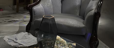 A living room with a large flat-screen TV mounted on the wall, a dark wooden armchair, a glass coffee table with a decorative object, and a small side table.