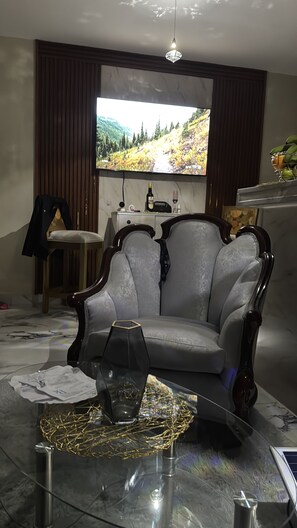 Un saló amb una gran televisió plana penjada a la paret, un sofà armari de fusta fosca, una taula de centre de vidre amb un objecte decoratiu i una petita taula auxiliar.