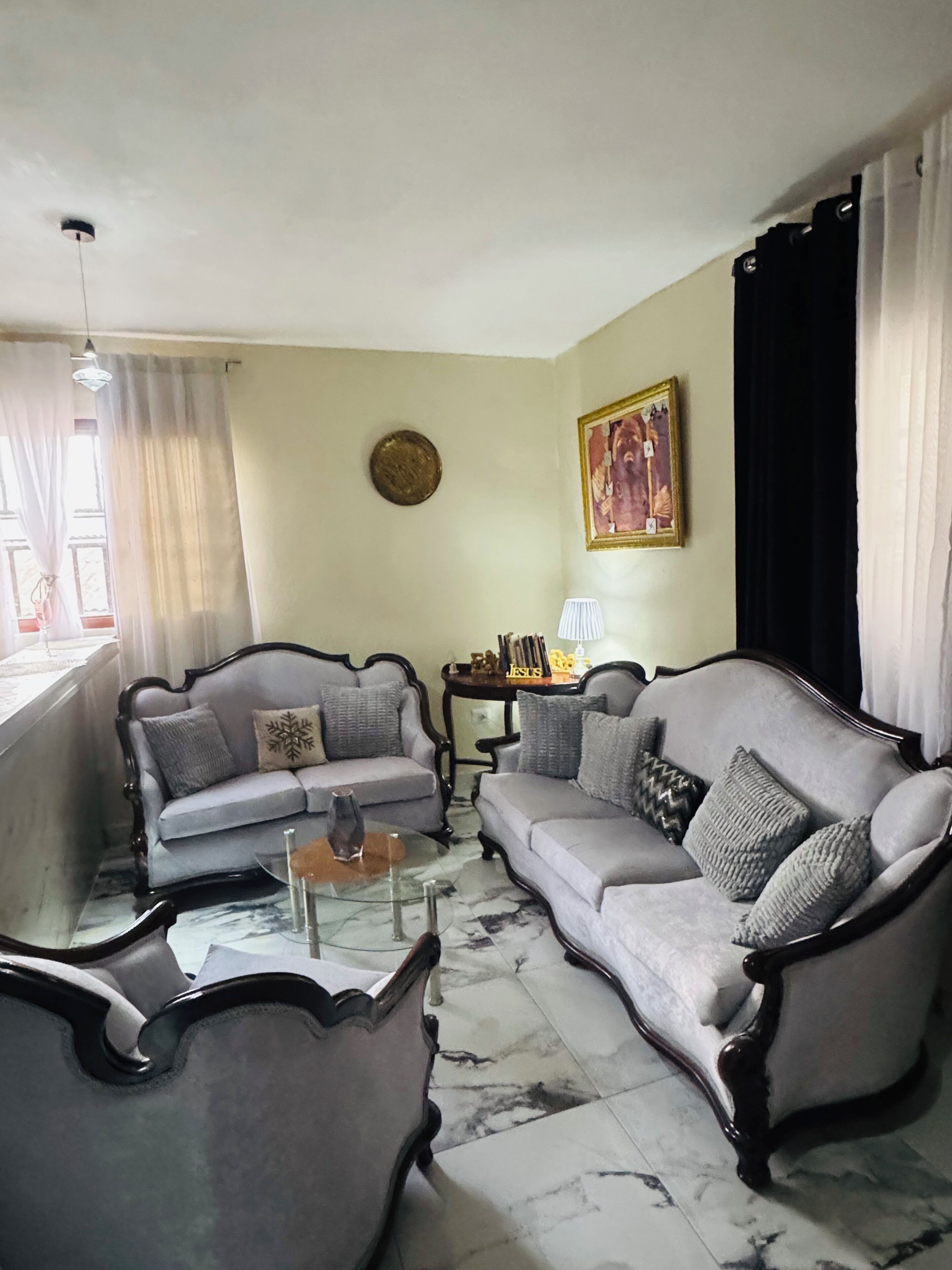 A living room with two grey sofas, a coffee table, and a lamp. There is a painting on the wall and a round decorative plate.