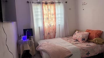 Ein Schlafzimmer mit einem Bett, einem Schreibtisch mit Computer, einer Klimaanlage und einem Fenster mit Vorhängen.
