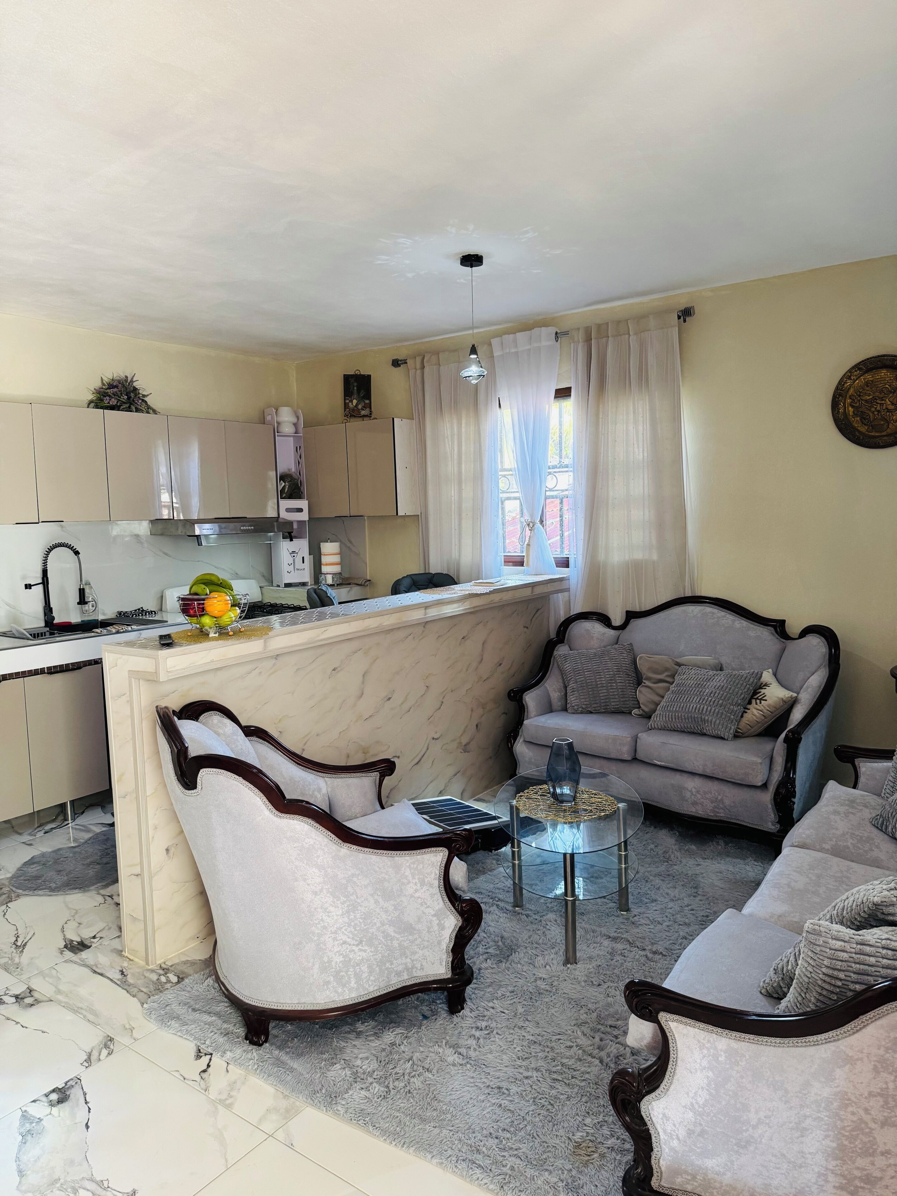 Ein Wohnzimmer mit einer Couch, Sesseln, einem Couchtisch und einer Küchenzeile mit Schränken und einer Spüle.