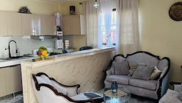 Ein Wohnzimmer mit einer Couch, Sesseln, einem Couchtisch und einer Küchenzeile mit Schränken und einer Spüle.